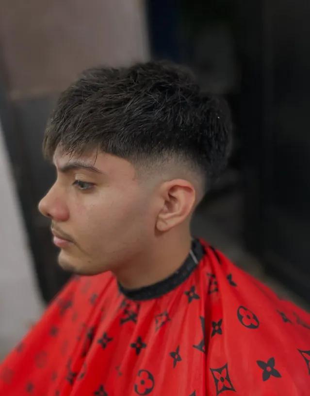 Perfil de un cliente recién cortado: fade cerrado sobre las patillas y flequillo texturado, con capa roja.