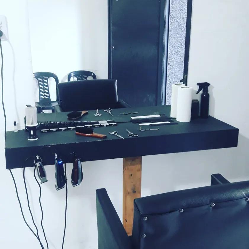 Mesada de trabajo negra con tijeras, peines y navaja alineados, y tres máquinas de cortar colgadas del borde.